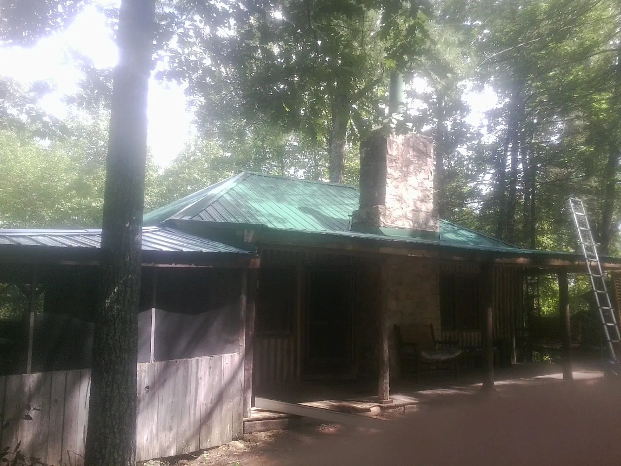 Green metal roof and stone chimney above a log cabin porch in Arlington